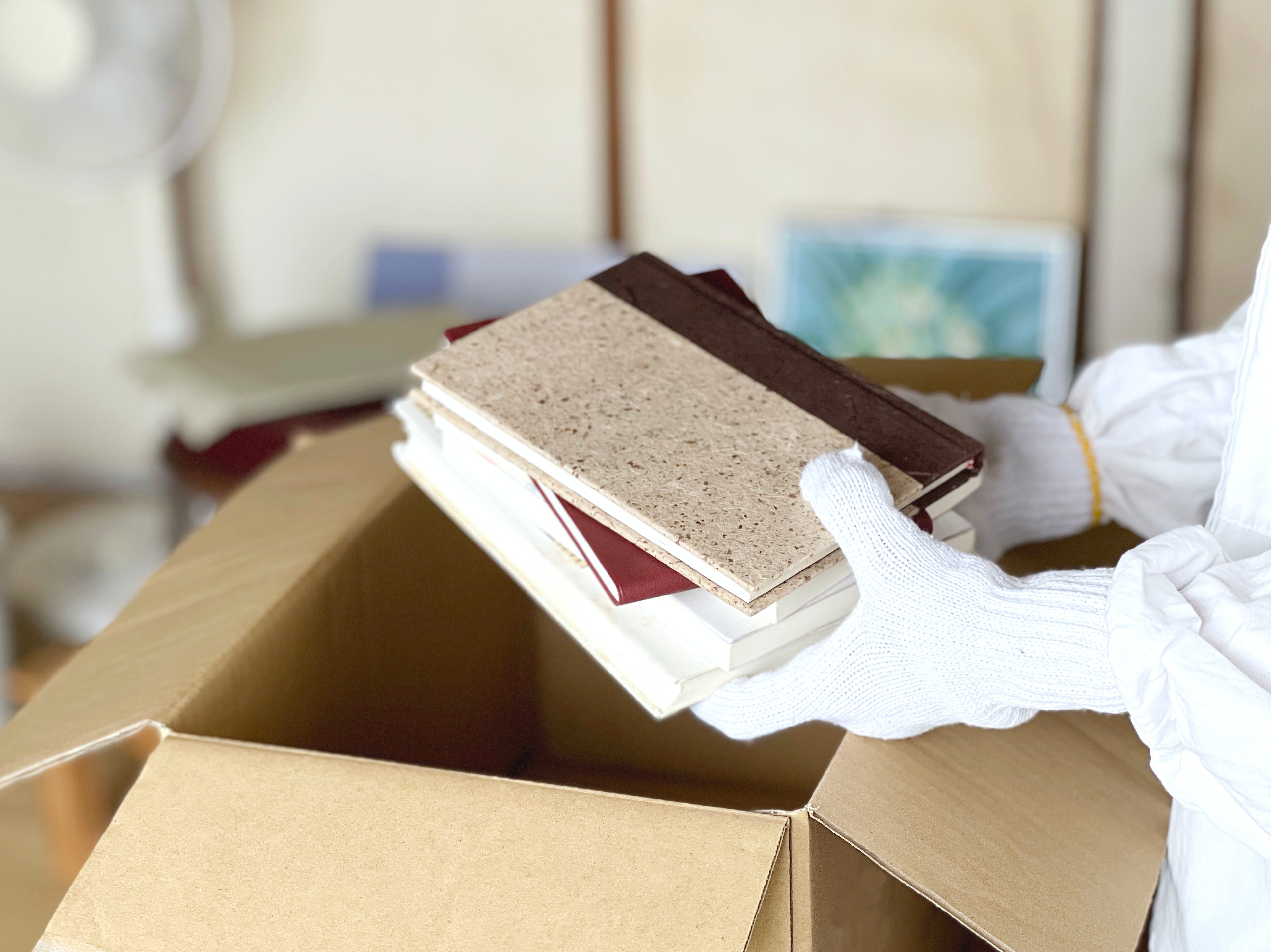 ダンボール箱に本などを入れる軍手をした手と